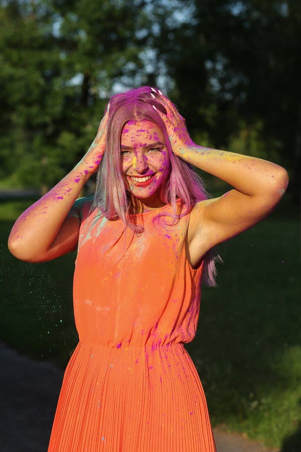 Charming blonde model posing covered with a colorful dry paint a. Charming blonde woman posing covered with a colorful dry paint at the park stock photography